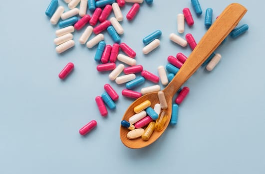 Various bright pills on a blue background lie in a wooden spoon against the background of different bright pills. Health care concept.
