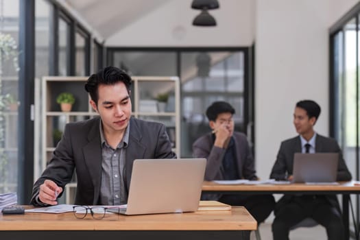 Portrait of confident young businessman using laptop while colleague in background
