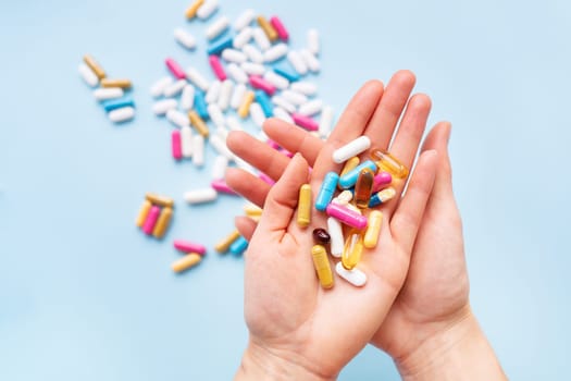 The girl holds a handful of bright vitamins in her palms against the background of other bright capsules. Concept of medicine and healthcare.