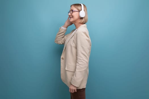 50s a woman in a jacket masters the technique for listening to music in headphones on a studio background