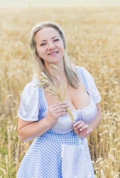 beautiful blonde with big breasts holds spikelets in a wheat field