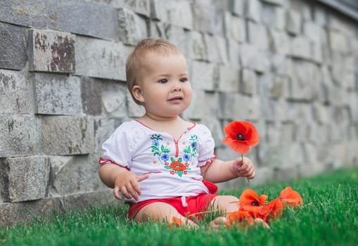 baby in embroidered shirt sitting on a lawn with flowers