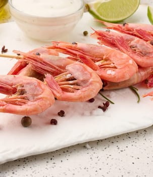 Shrimps strung on wooden sticks, soy sauce and spices on a white table, top view