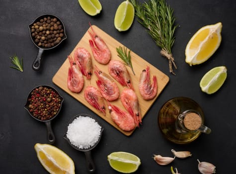 Boiled shrimp on a board, lemon slices, spices on a black background, top view