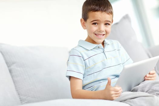 This is fun. Image of a little boy sitting on the sofa and playing games on a digital tablet.