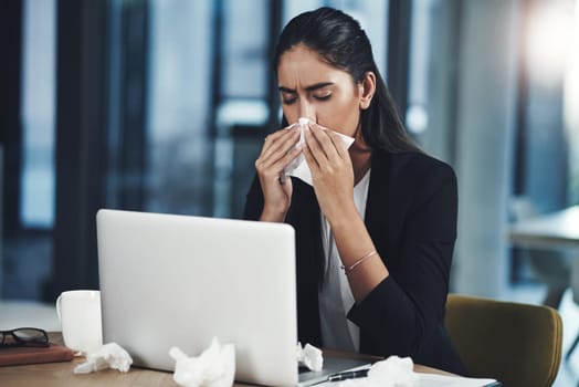 Flu in the workplace can cause significant reduction in productivity. a young businesswoman blowing her nose while working in an office.