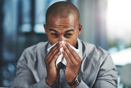 This flu is negatively impacting on my success. Portrait of a young businessman blowing his nose in an office.