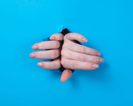 Female hands sticking out through a hole on a blue background.