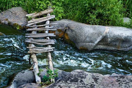 Wooden old bridge made of two logs and boards across a raging stream, stones