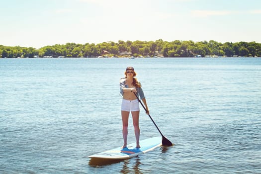Its my definition of fun. an attractive young woman paddle boarding on a lake.