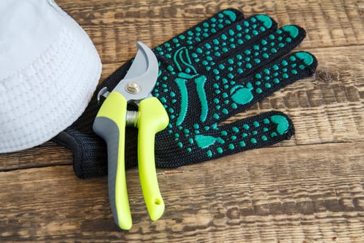 Garden glove, pruner and hat on wooden boards.