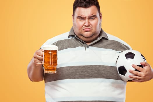 Soccer fun - sad and fat man at oktoberfest, taking beer and soccer ball on yellow background.