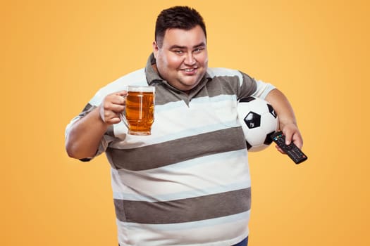 Soccer fun - happy and fat man at oktoberfest, taking beer and soccer ball on yellow background.