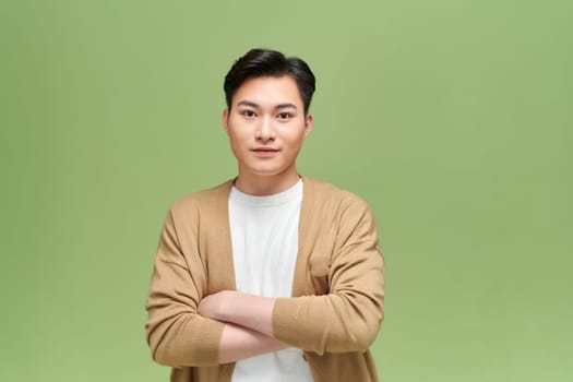 Portrait of a handsome young man looking at camera, serious expression, isolated on green background.