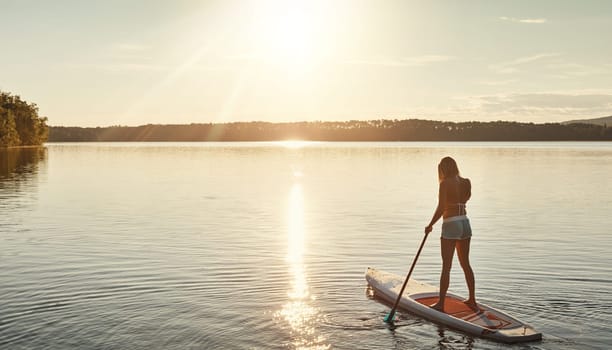 Gone paddling. an attractive young woman paddle boarding on a lake.