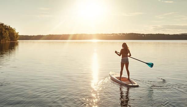 My happy place. an attractive young woman paddle boarding on a lake.