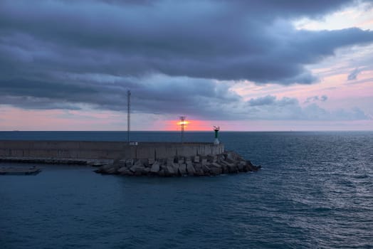 Sunrise from green lighthouse on maritime breakwater