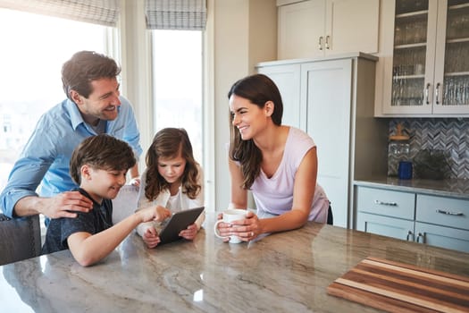Technology keeps them close. a married couple and their young children playing with a tablet together in their kitchen.