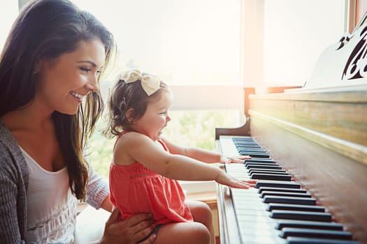 Piano lessons with Mom are always fun. a mother watching her adorable little daughter playing the piano at home.