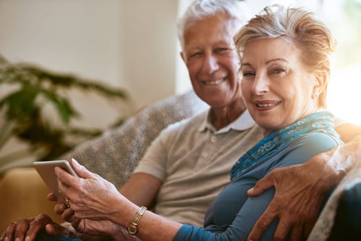 Our home is technology friendly. Portrait of a happy senior couple using a digital tablet together on the sofa at home