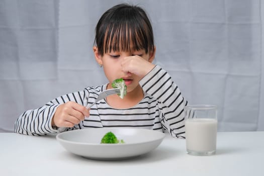 Children don't like to eat vegetables. Cute Asian girl refusing to eat healthy vegetables. Nutrition and healthy eating habits for children.