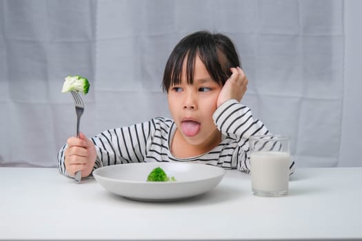 Children don't like to eat vegetables. Cute Asian girl refusing to eat healthy vegetables. Nutrition and healthy eating habits for children.