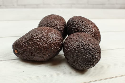 Four brown whole avocados on white boards.