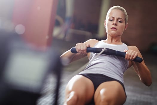 Learn to love the burn. a young woman working out on a rowing machine in a gym.
