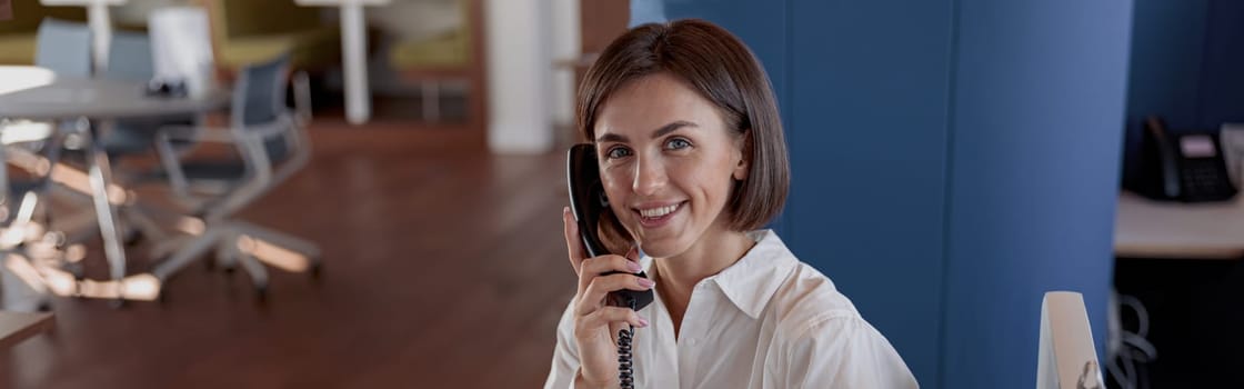 Smiling european woman worker talk phone with client sit on her workplace in office