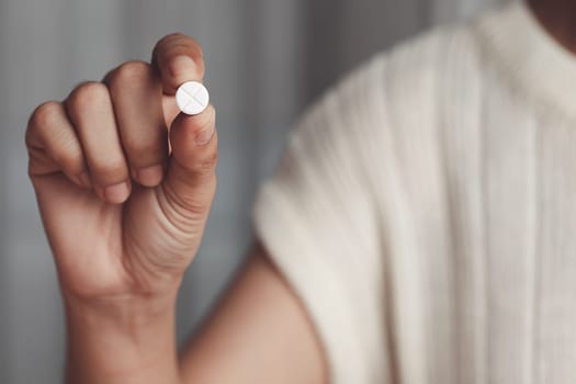 Asian woman's hand holding a white pill for medical and healthcare concept.