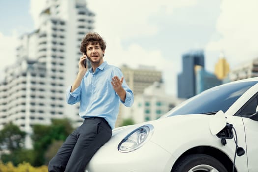 Progressive businessman talking on the phone with recharging electric vehicle.