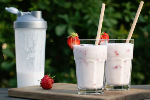 Protein shake from yogurt and strawberries in a shaker and two glass glasses on a wooden table