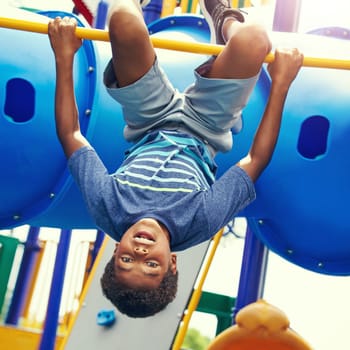 See life from a childs perspective. a young boy hanging upside down on a jungle gym in the park.