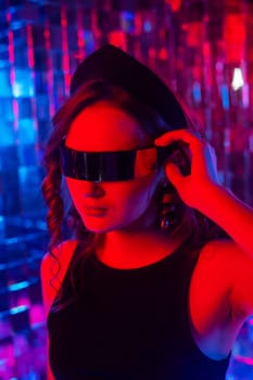 Close-up portrait of a caucasian woman in sunglasses in neon light against a mirror wall.