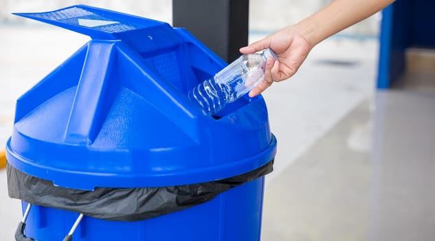 Close up woman hand throwing empty plastic water bottle into recycling bin