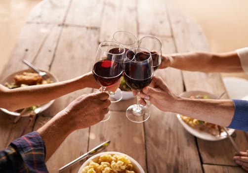 Hands, group and wine glass for toast at table for celebration, food and friends at lunch event. People, together and celebrate with alcohol, glasses and support at party, dinner and family home