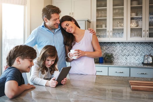 Technology has improved their parenting experience. a married couple and their young children playing with a tablet together in their kitchen.