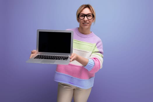 attractive blond woman freelancer with a laptop in her hands shows a screen mockup on a purple background