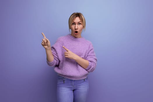 shocked blond young woman in a lilac sweater with her mouth open on a bright background