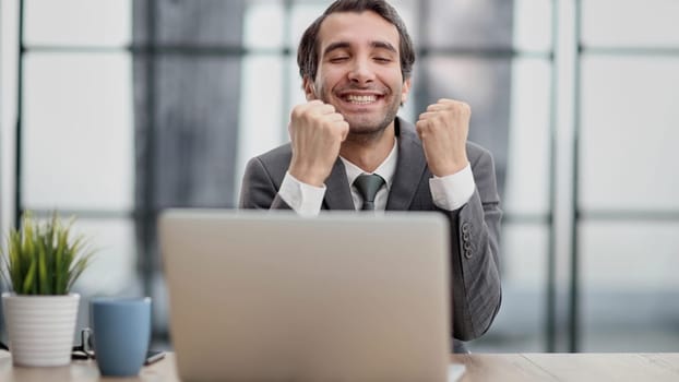 Excited businessman sitting at table with laptop and celebrating success