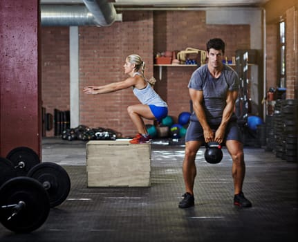 Dedicate yourself to a healthier you. two people working out with kettlebells in a gym.