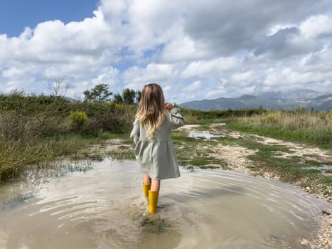 Little girl walks through a puddle to a country road and looks at the mountains