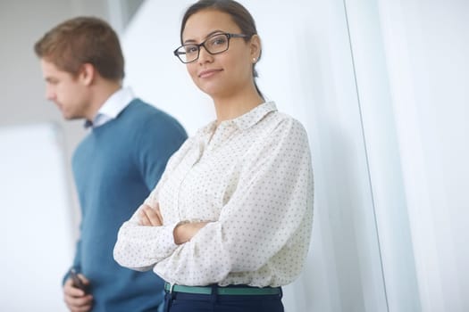 Taking success in stride. Portrait of an attractive young woman standing in an office with a coworker in the background.