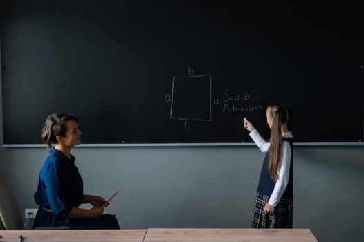Caucasian little girl answers the question of the female teacher at the blackboard.