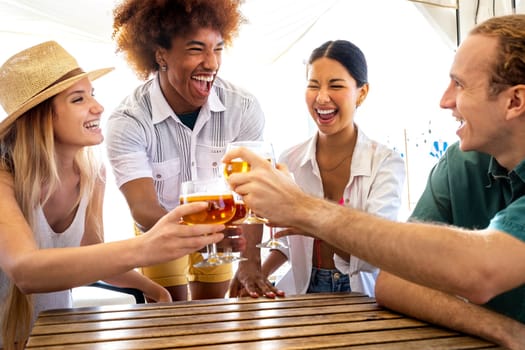 Young black man and his multiracial friends toasting with beer at a beach bar during summer vacation.