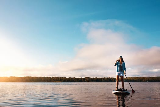 The best trips are the ones on water. a young woman paddle boarding on a lake.