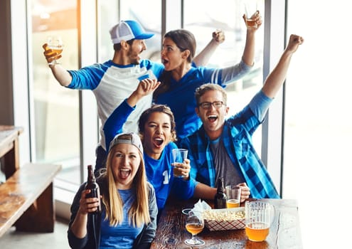 Whats a sport with out the support. a group of friends cheering while watching a sports game at a bar.