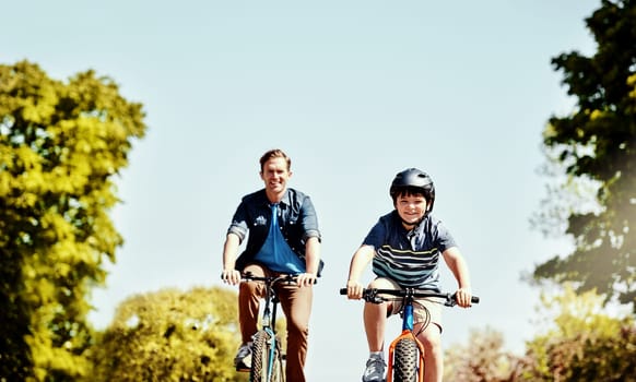 Enjoying the fresh air along their adventure. a young boy and his father riding together on their bicycles.