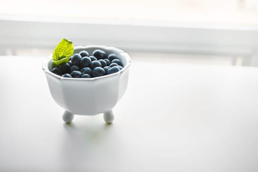 Tiny fruit with enormous health benefits. fresh blueberries in a bowl on a white table.