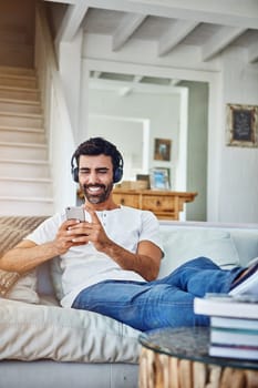 Great tunes to relax to. a man relaxing on the sofa while using his phone and headphones.